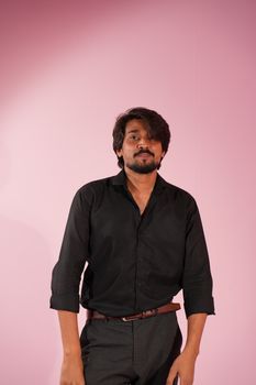 A confident young man in a black shirt posing against a pink backdrop.