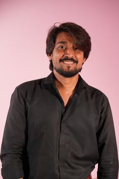 Portrait of a man in a black shirt smiling against a pink backdrop.