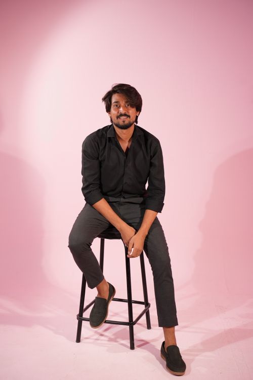 Free A man in casual black attire sits on a stool against a pink background, exuding a relaxed vibe in a studio setting. Stock Photo