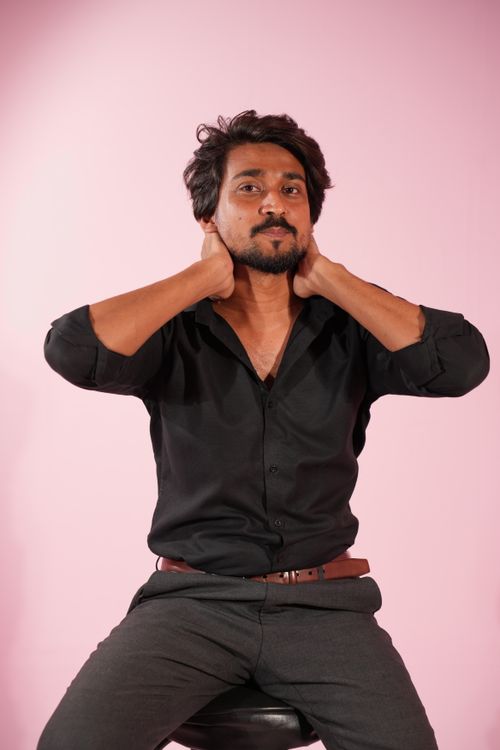 Free A relaxed man sitting in front of a pink backdrop wearing a black shirt, exuding confidence. Stock Photo