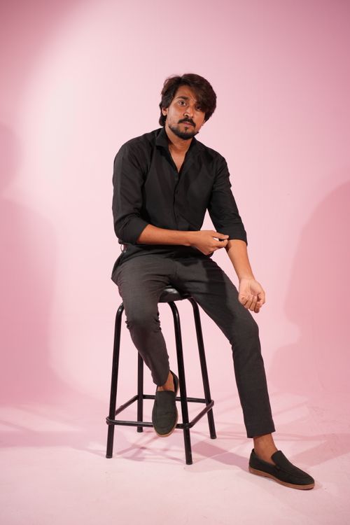 Free Man seated on a stool in stylish black outfit on pink background. Stock Photo