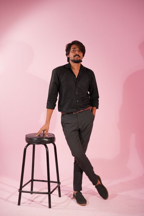 Free Young man in black attire poses confidently with a stool against a pink backdrop Stock Photo