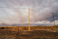 Unrecognizable distant person standing on empty rural road near utility poles against cloudy sky during sunset