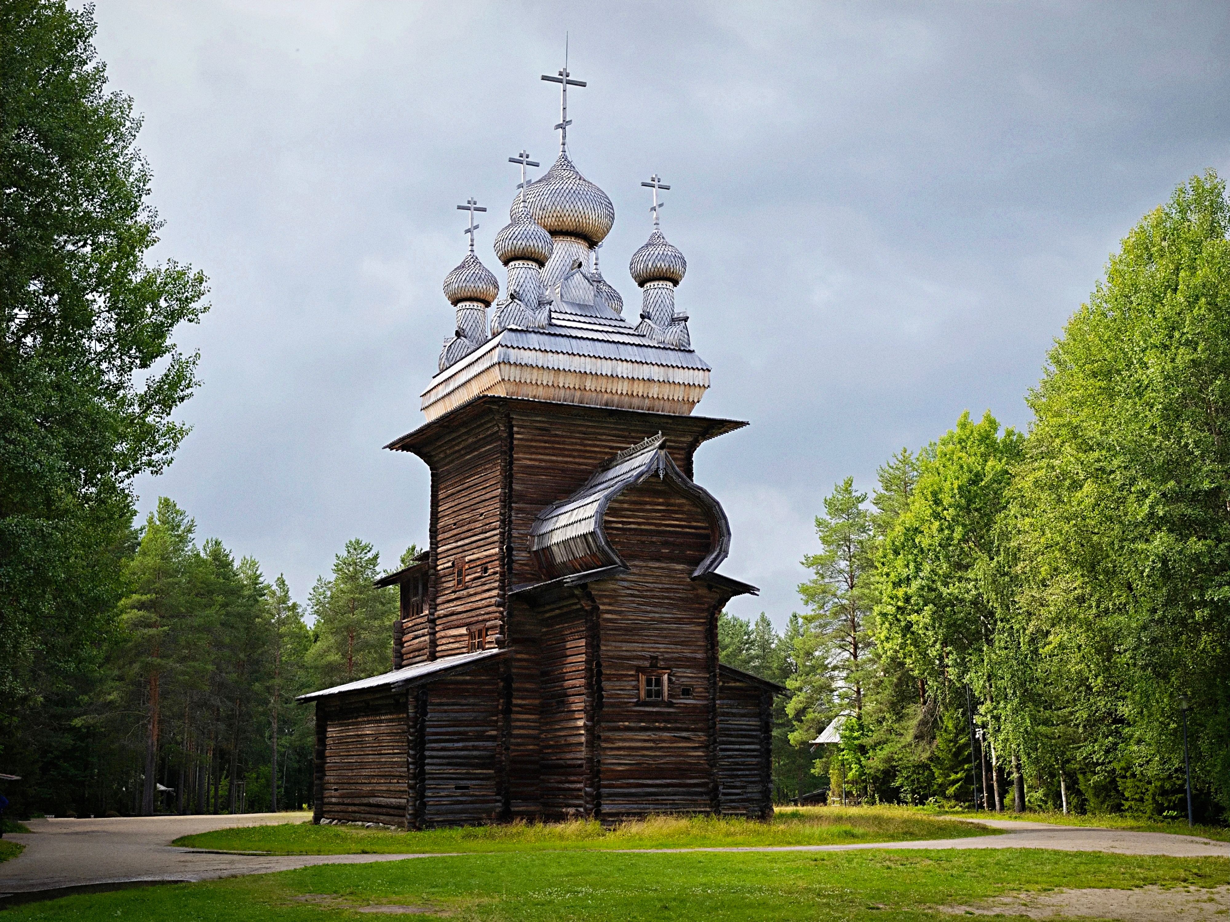 A historic Russian wooden church with iconic domes set in a lush forest landscape.