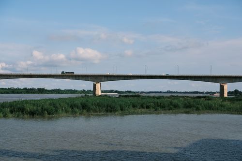 Free A tranquil riverside scene with a bridge stretching over calm waters under a clear blue sky. Stock Photo