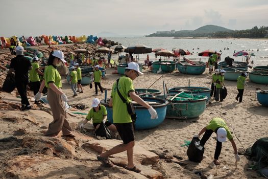 A group of volunteers in green shirts clean up trash on a beach, promoting environmental awareness.