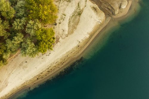 Free Stunning aerial photo capturing a serene beach, lush green trees, and clear turquoise water. Stock Photo