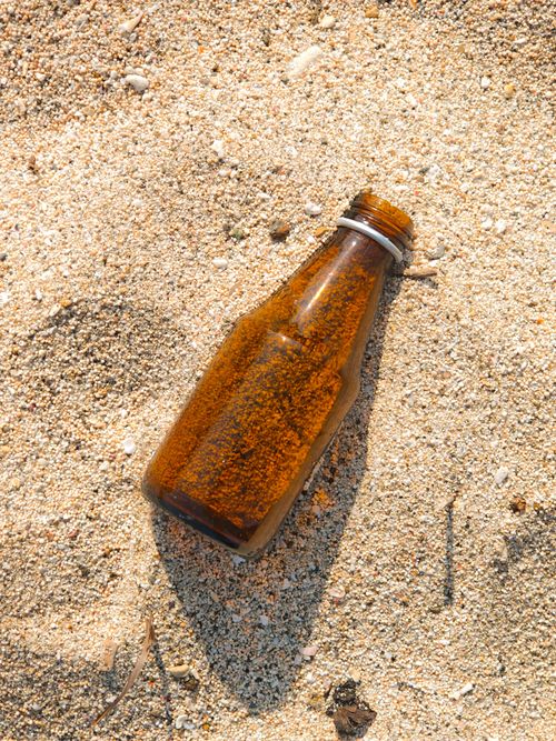 Free A brown glass bottle partially buried in sand on a sunny beach, highlighting environmental issues. Stock Photo