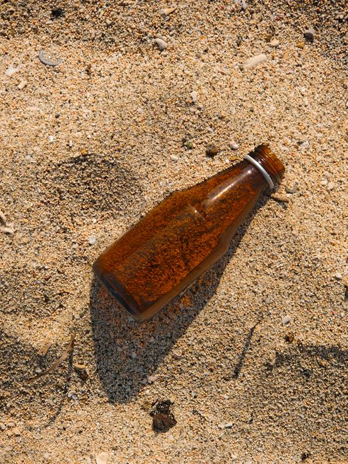 Free Glass bottle lying on sandy beach symbolizing marine pollution and environmental concern. Stock Photo