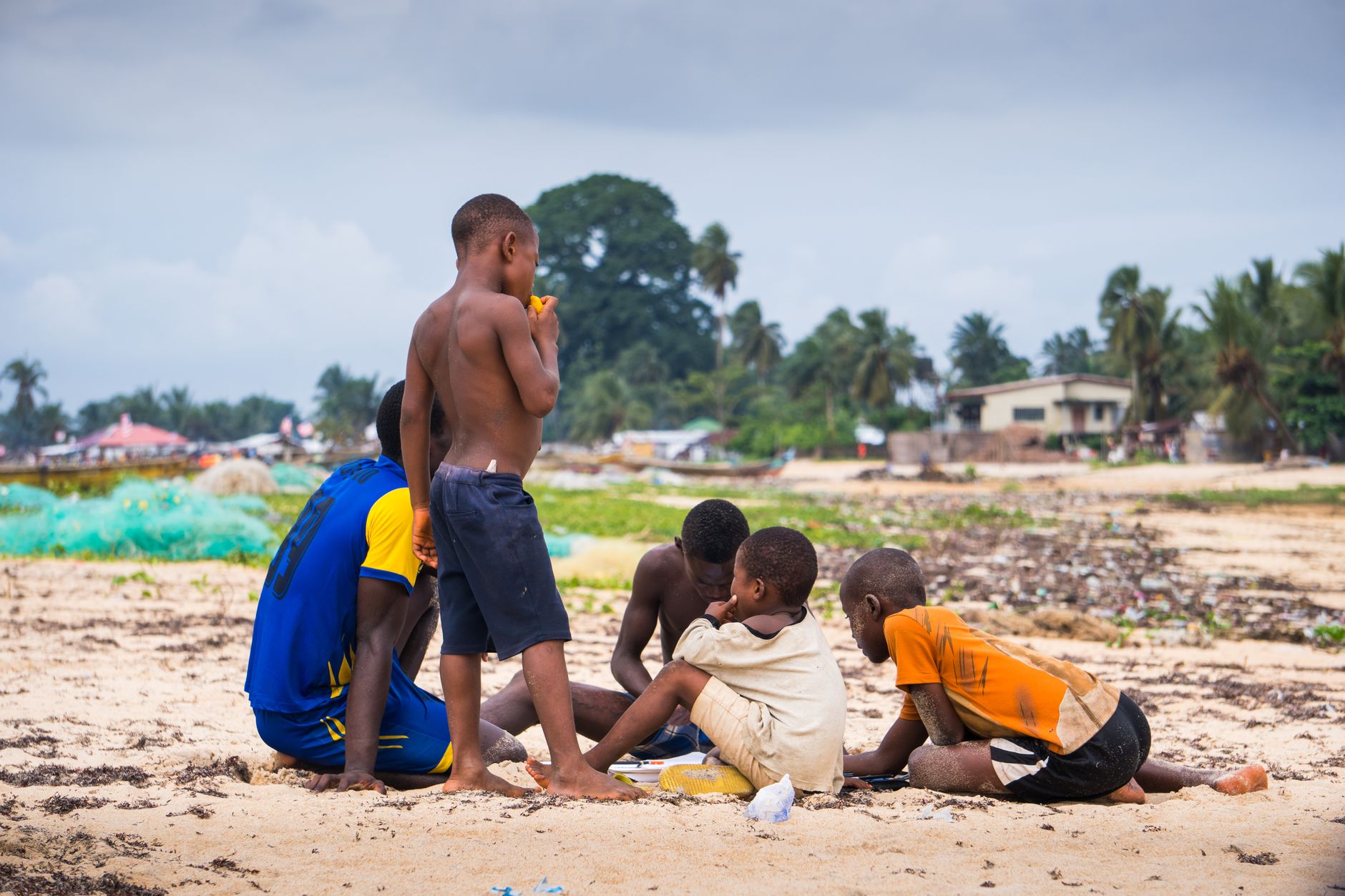 Group of boys playing on a sandy beach near a fishing village in Liberia.