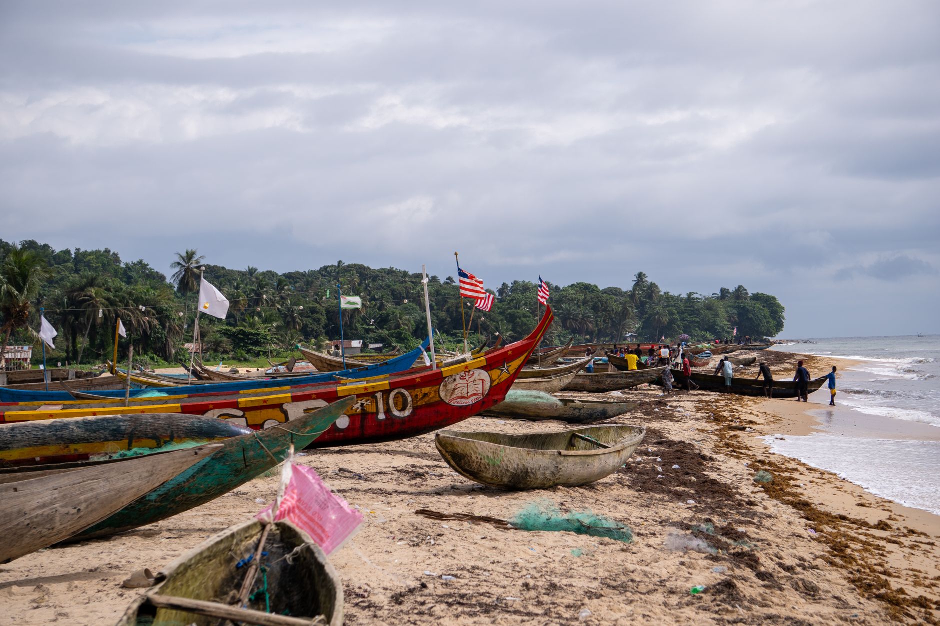 Colorful wooden fishing boats line the sandy beach in Robertsport, Liberia, amidst a vibrant coastal village scene.