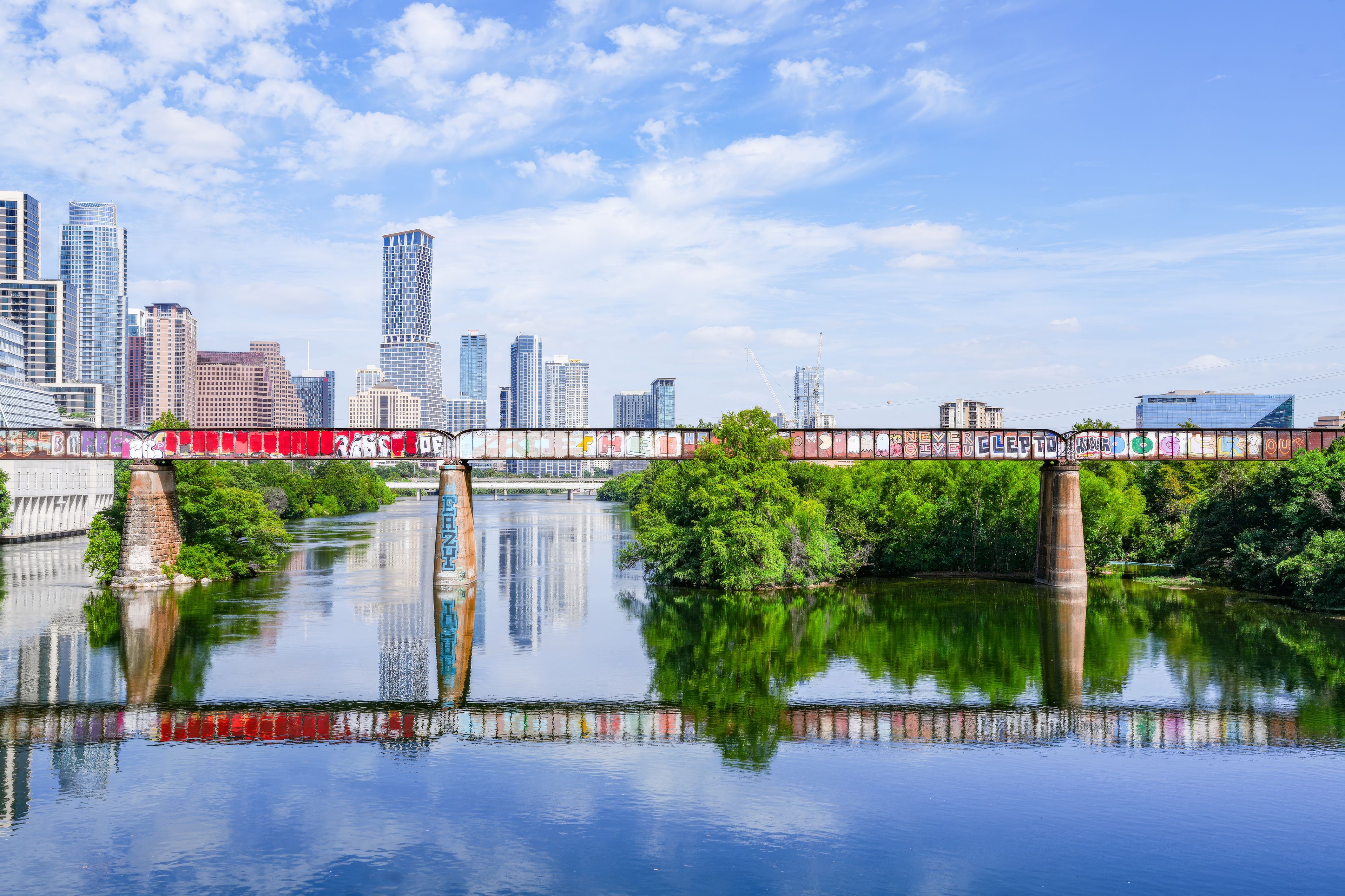Vibrant cityscape of Austin with graffiti-covered bridge over a reflective river.