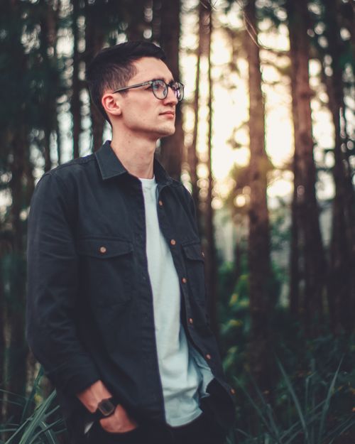 Free Portrait of a man in eyeglasses and jacket, in a serene forest setting. Stock Photo