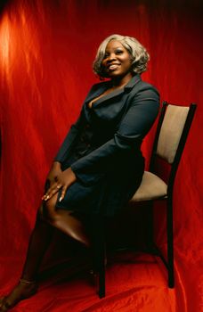 Confident woman in a navy dress poses against a vibrant red backdrop, exuding elegance and style.