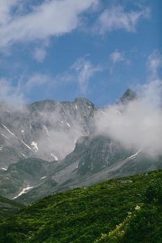 Breathtaking view of a mountain range under a blue sky with misty clouds encircling the peaks.