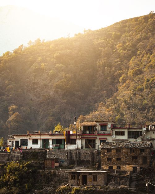 Free Charming Indian mountain village aglow in sunrise light, highlighting traditional homes and lush hillside. Stock Photo