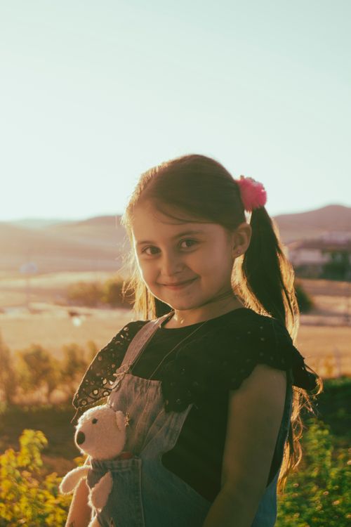 Free Portrait of a young girl outdoors holding a teddy bear with a warm, sunlit background. Stock Photo