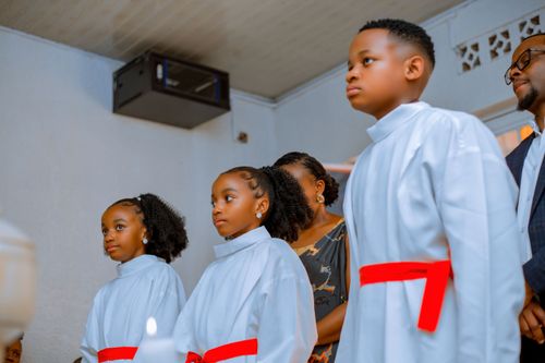 Free Children in white robes with red sashes attend church ceremony indoors. Stock Photo