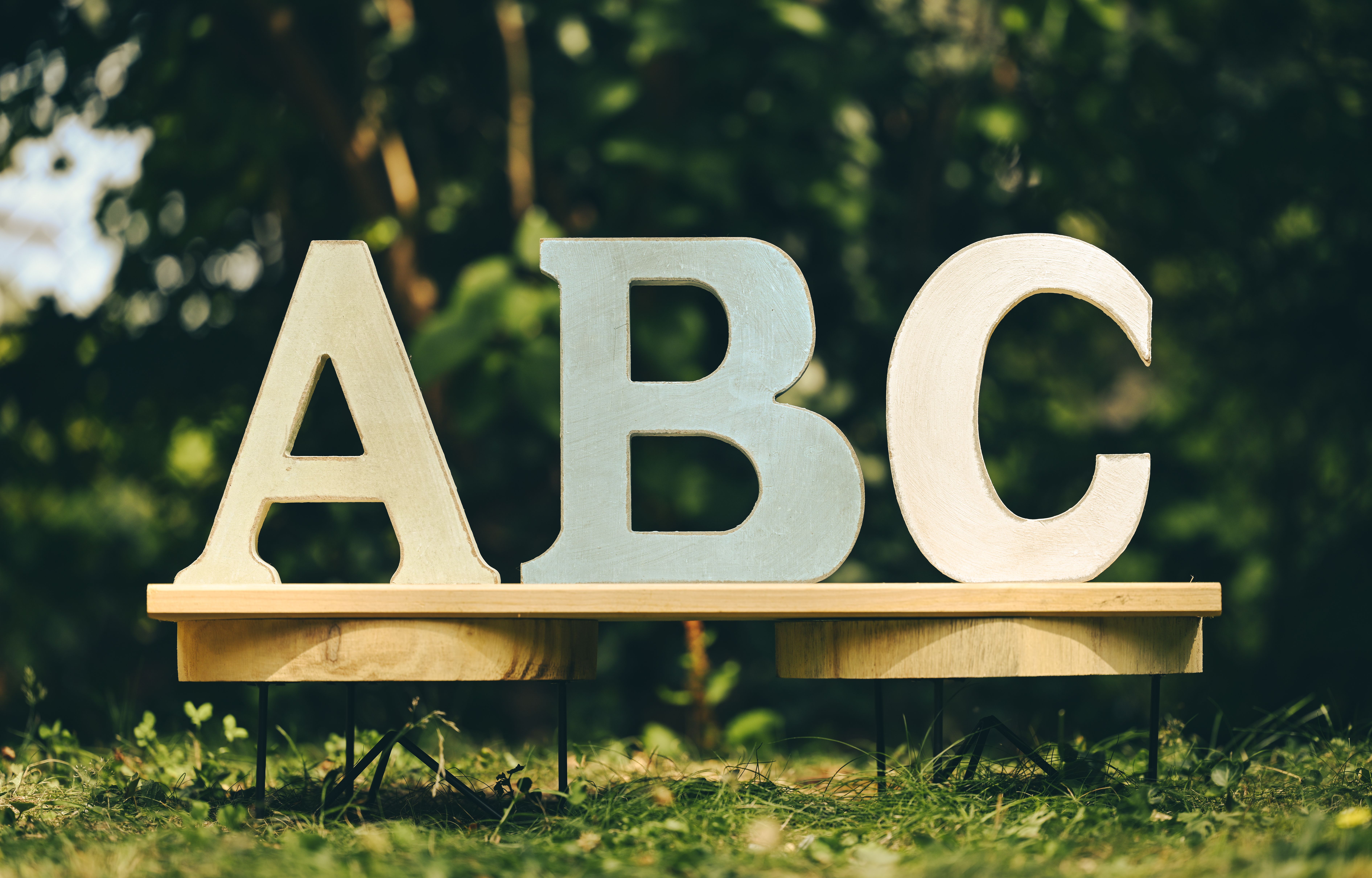 Large decorative letters A, B, C standing on a wooden stand outdoors in a sunny garden setting.