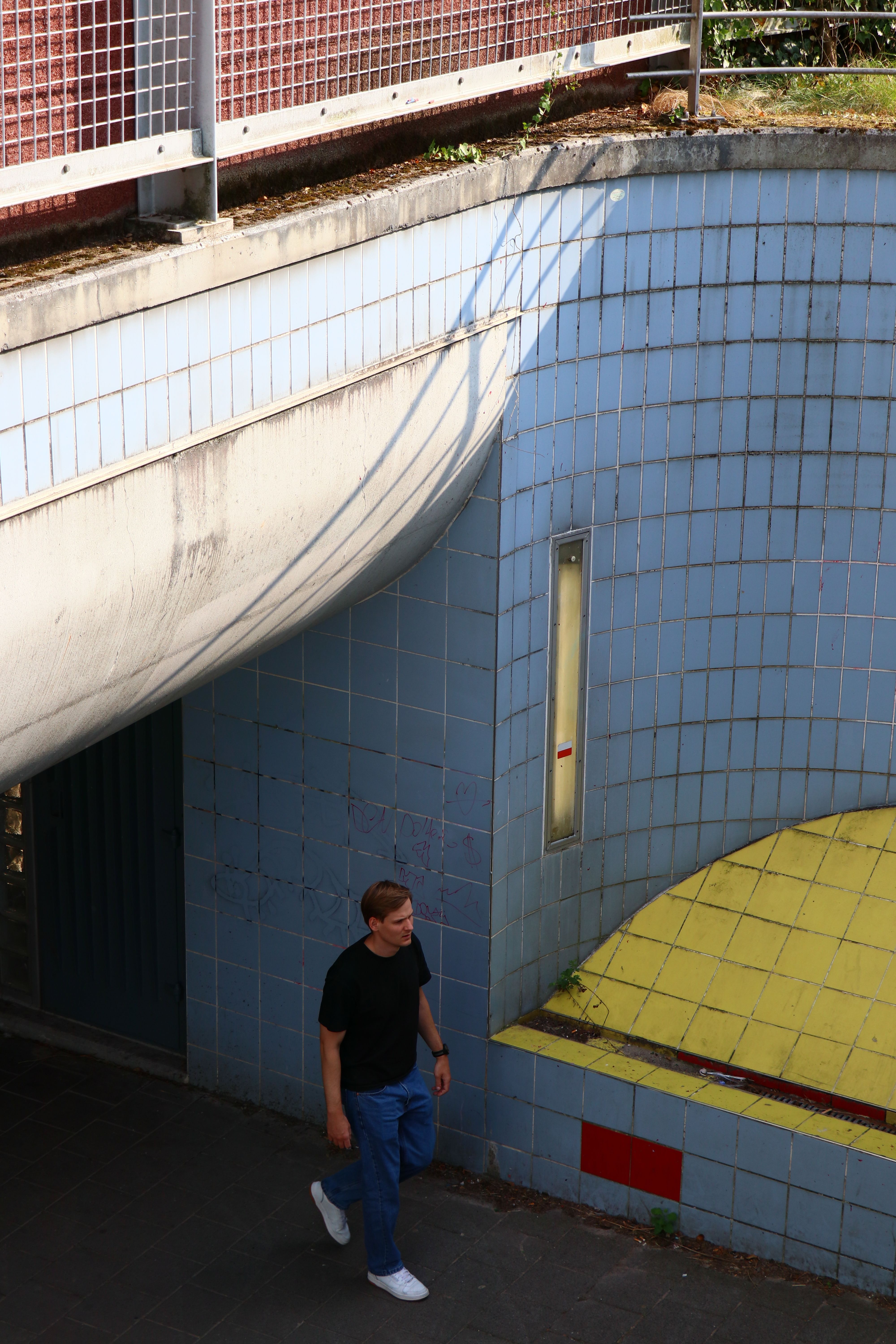 A man walks through a tiled underpass, reflecting urban life and architecture.