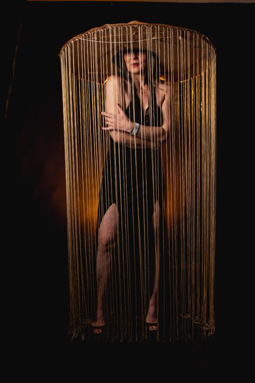 Free Creative portrait of a woman wearing a hat with long fringes, standing against a dark background. Stock Photo