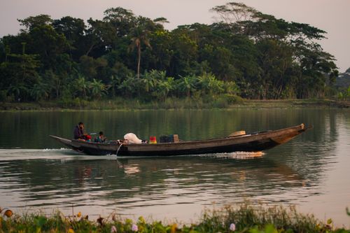 Free Peaceful scene of a traditional boat on a calm river at sunset, surrounded by lush tropical vegetation. Stock Photo
