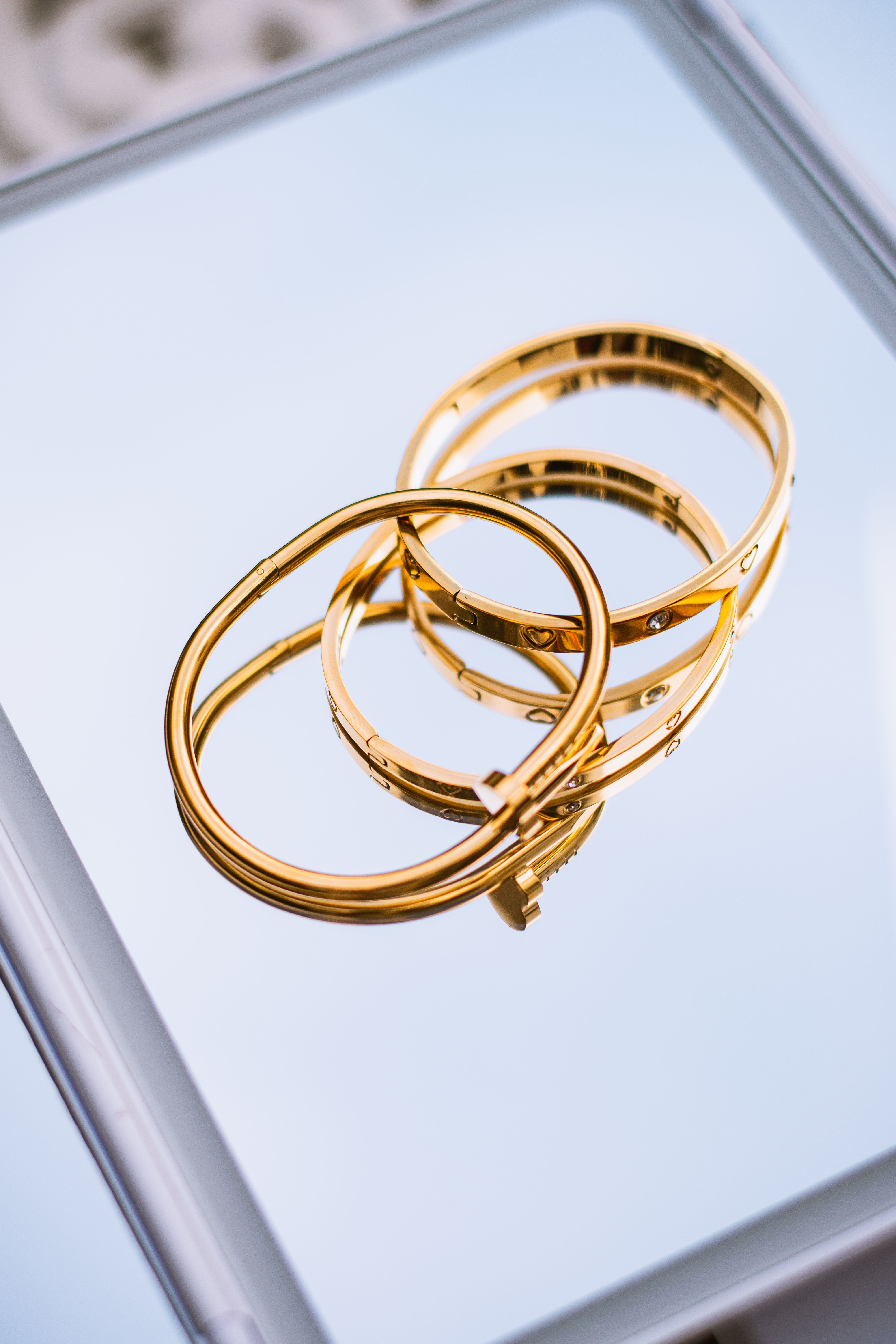 Three elegant gold bracelets arranged on a reflective surface