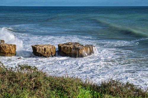 Free Waves crash over rugged coastal rocks on a bright, breezy day, capturing the power of nature. Stock Photo