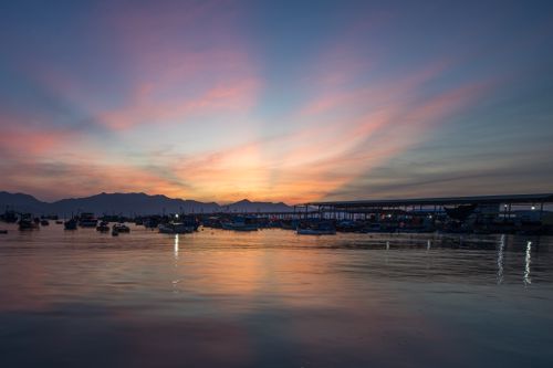 Free Calm evening at the harbor with boats silhouetted against a vibrant sunset sky. Stock Photo