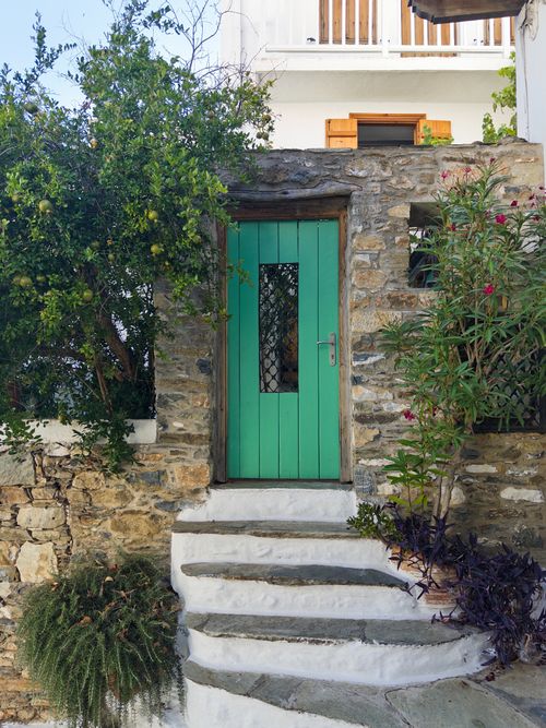 Free A rustic green door set in a stone wall with lush plants, evoking a Greek village charm. Stock Photo