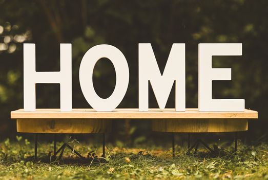 Artistic display of wooden letters spelling 'HOME' on a bench outdoors.