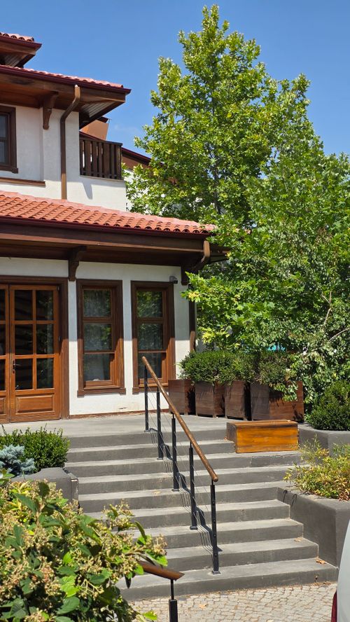 Free A picturesque two-story house with a red tiled roof, surrounded by lush greenery and a garden. Stock Photo