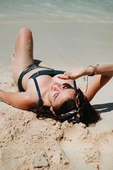 A woman enjoying a sunny day, sunbathing on a sandy beach with turquoise water.