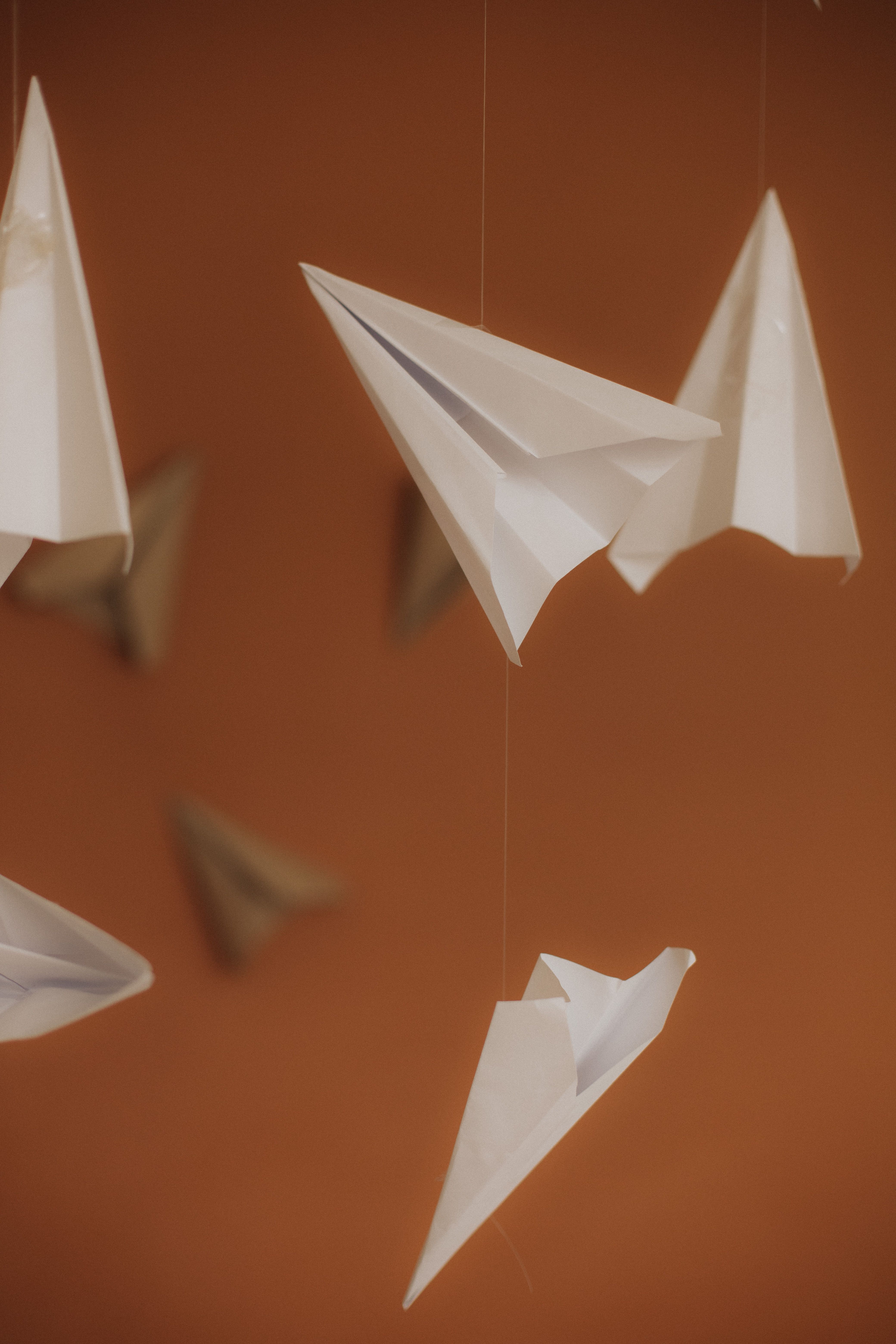 Artistic display of white paper airplanes floating against a warm orange backdrop.