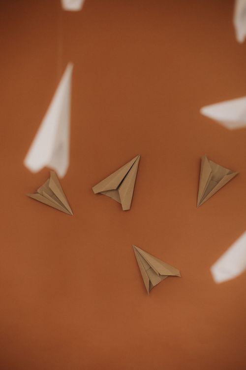 Free Creative display of floating paper airplanes on a bold orange backdrop. Stock Photo