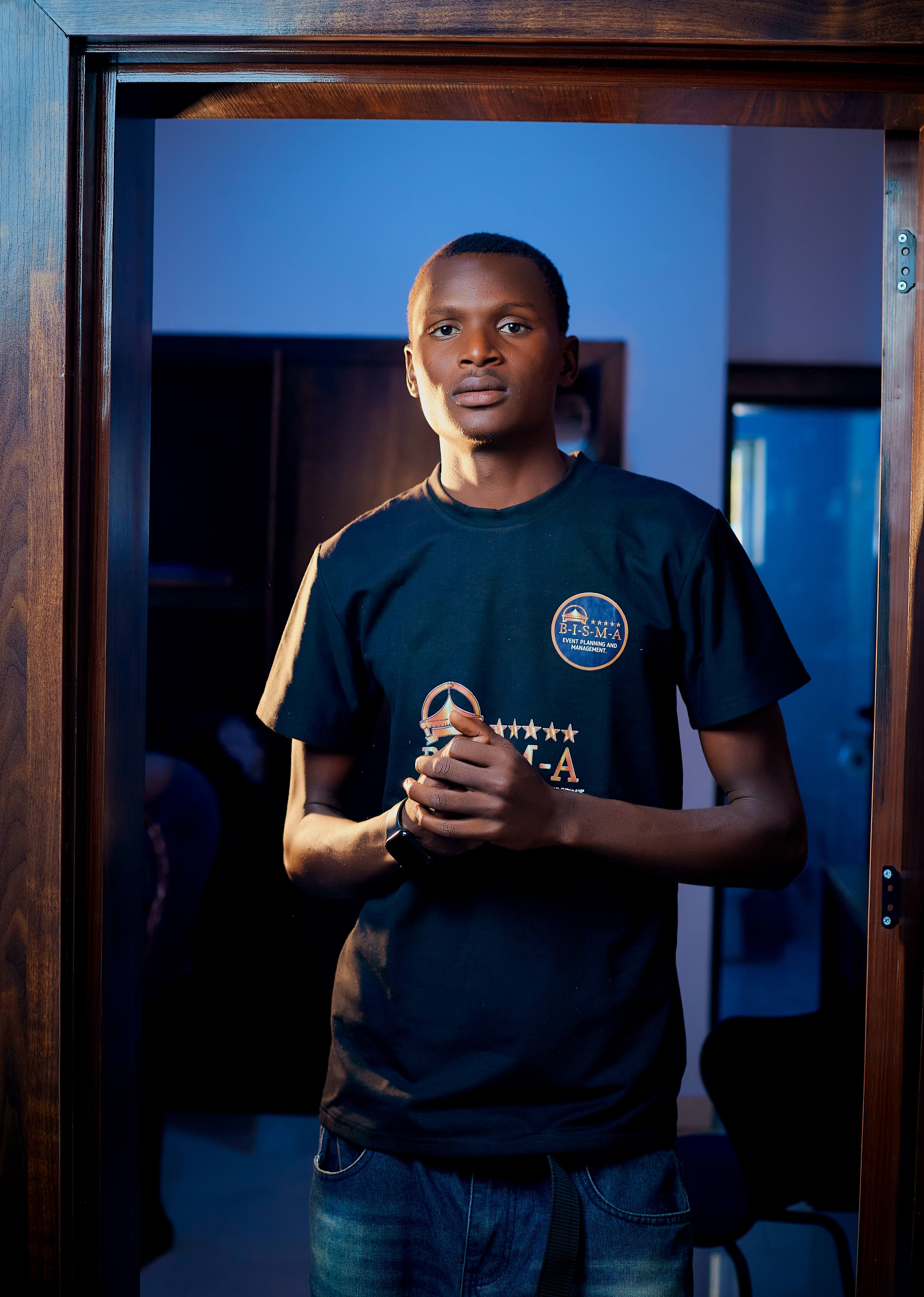 Portrait of a young man standing in an indoor doorway, illuminated by blue lighting.