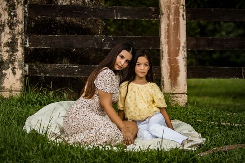 Free A serene outdoor portrait of a mother and daughter seated on grass, bonding in summer. Stock Photo