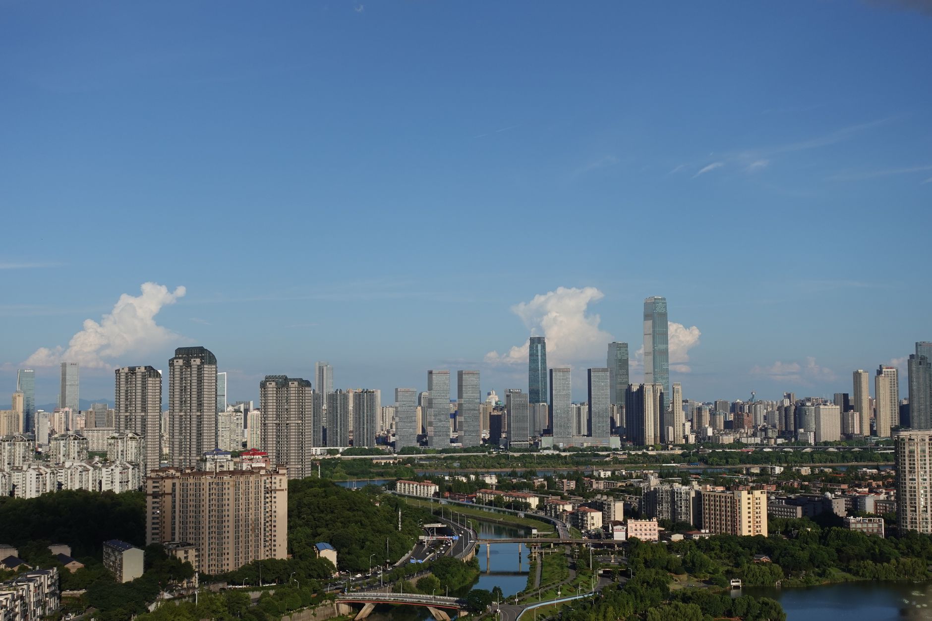 A stunning aerial view of a modern city skyline under a clear blue sky with scattered clouds. — free online jigsaw puzzle on JigsawPuzzlesFreeOnline.org