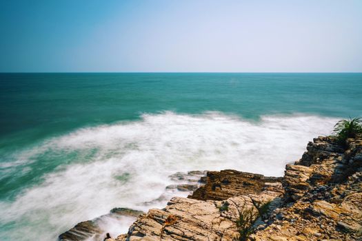 Stunning view of ocean waves crashing against a rocky shoreline under a clear sky.