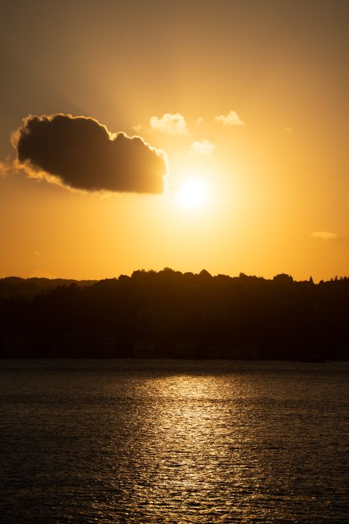 Free Stunning sunset view with golden hues reflecting over the calm ocean waters against a silhouetted horizon. Stock Photo
