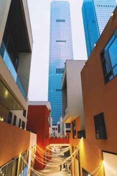 Charming urban alleyway with string lights against towering skyscrapers at dusk.