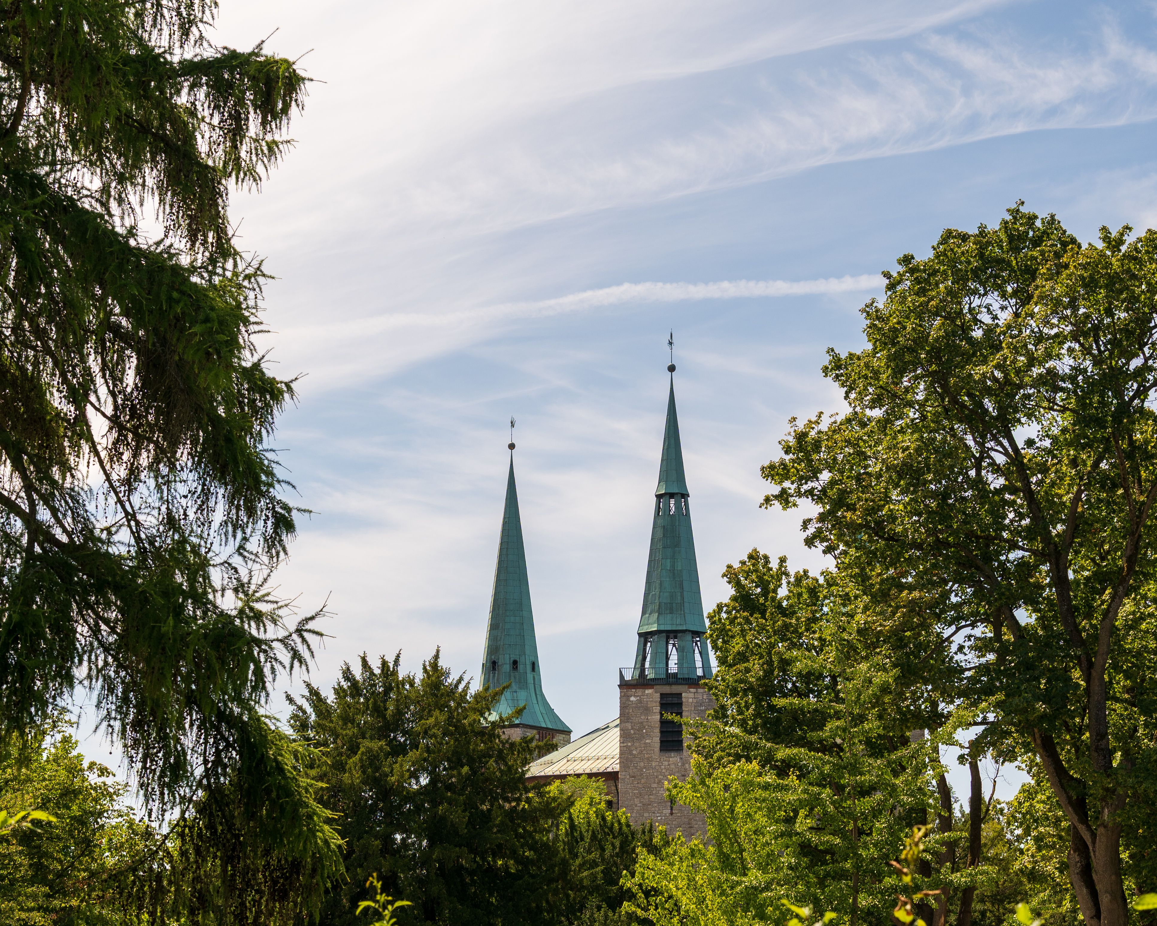 Two tall church spires rise above the lush trees against a clear sky, capturing a serene summer day.
