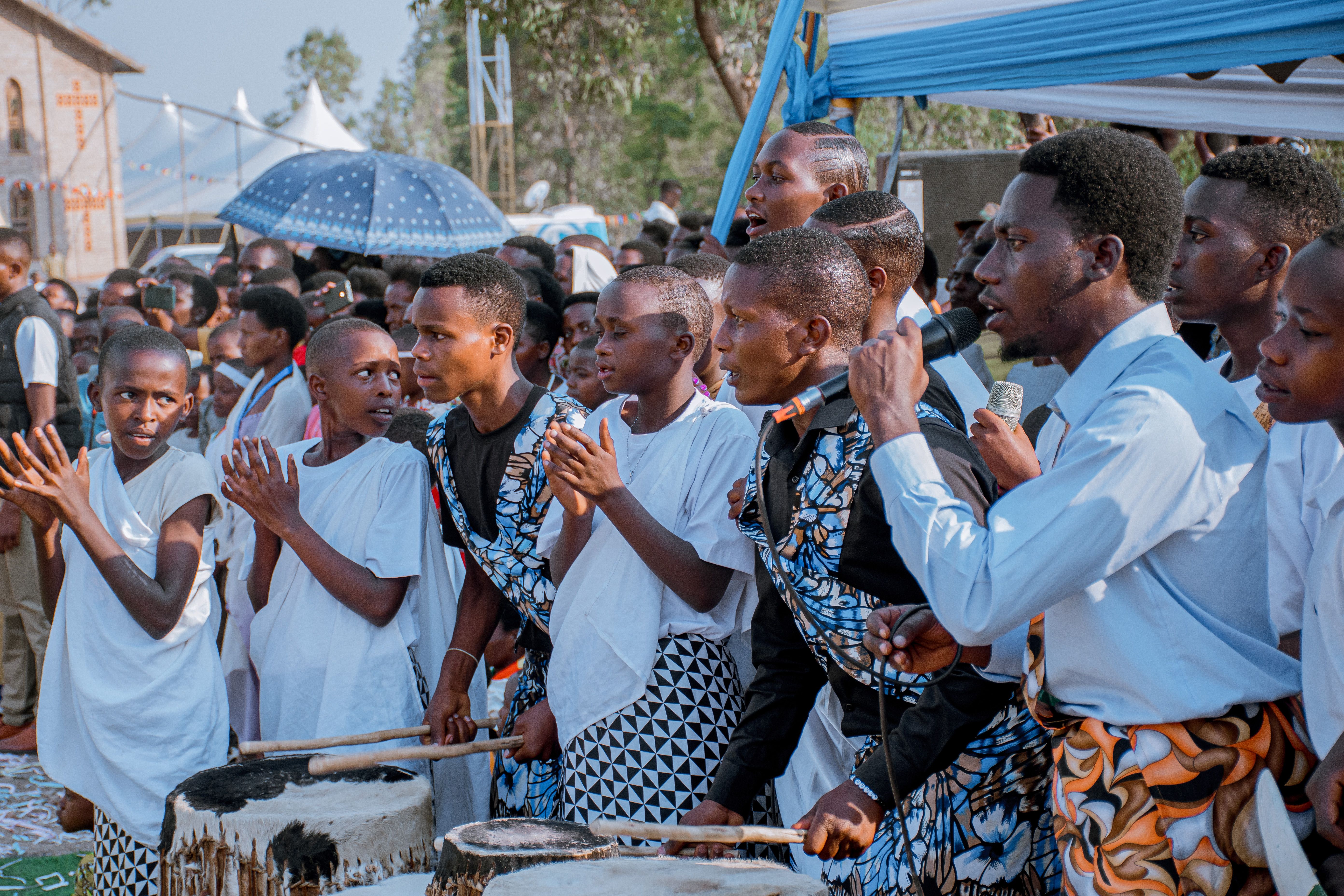 A vibrant group of Rwandan youth engaging in a cultural drumming and singing ceremony outdoors.