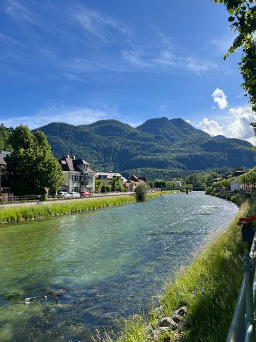 Free Tranquil river view with lush mountains and quaint village houses under a clear blue sky. Stock Photo