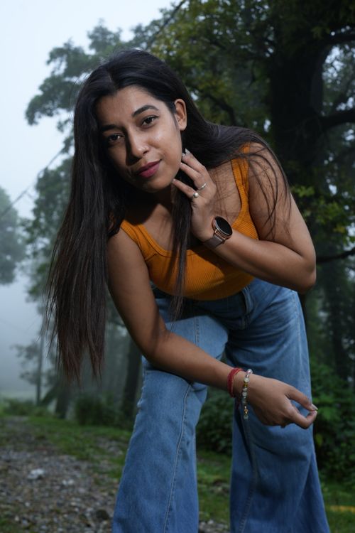 Free Young woman in casual jeans and orange top posing outdoors with trees in the background. Stock Photo