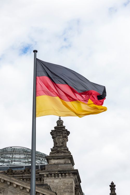 Free German flag waving at the Reichstag, Berlin under a cloudy sky. Stock Photo
