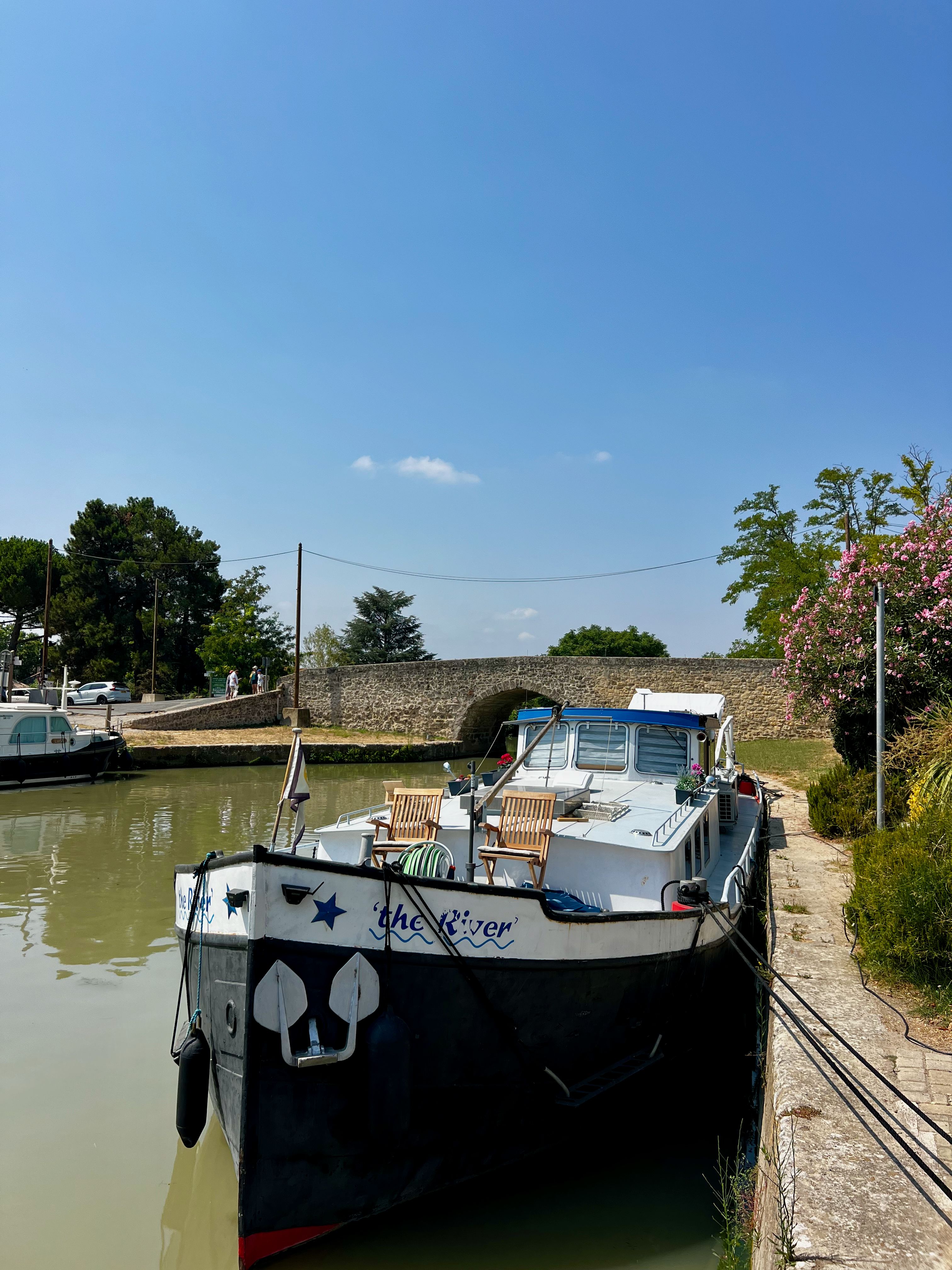 A picturesque boat moored on a serene canal, surrounded by greenery and clear blue skies.