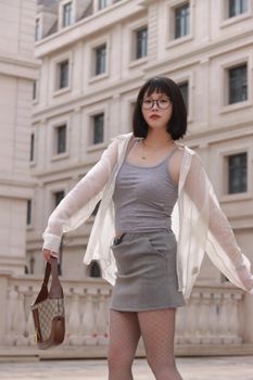 Stylish woman with glasses and skirt posing in Nanjing, China. Urban fashion and elegance.
