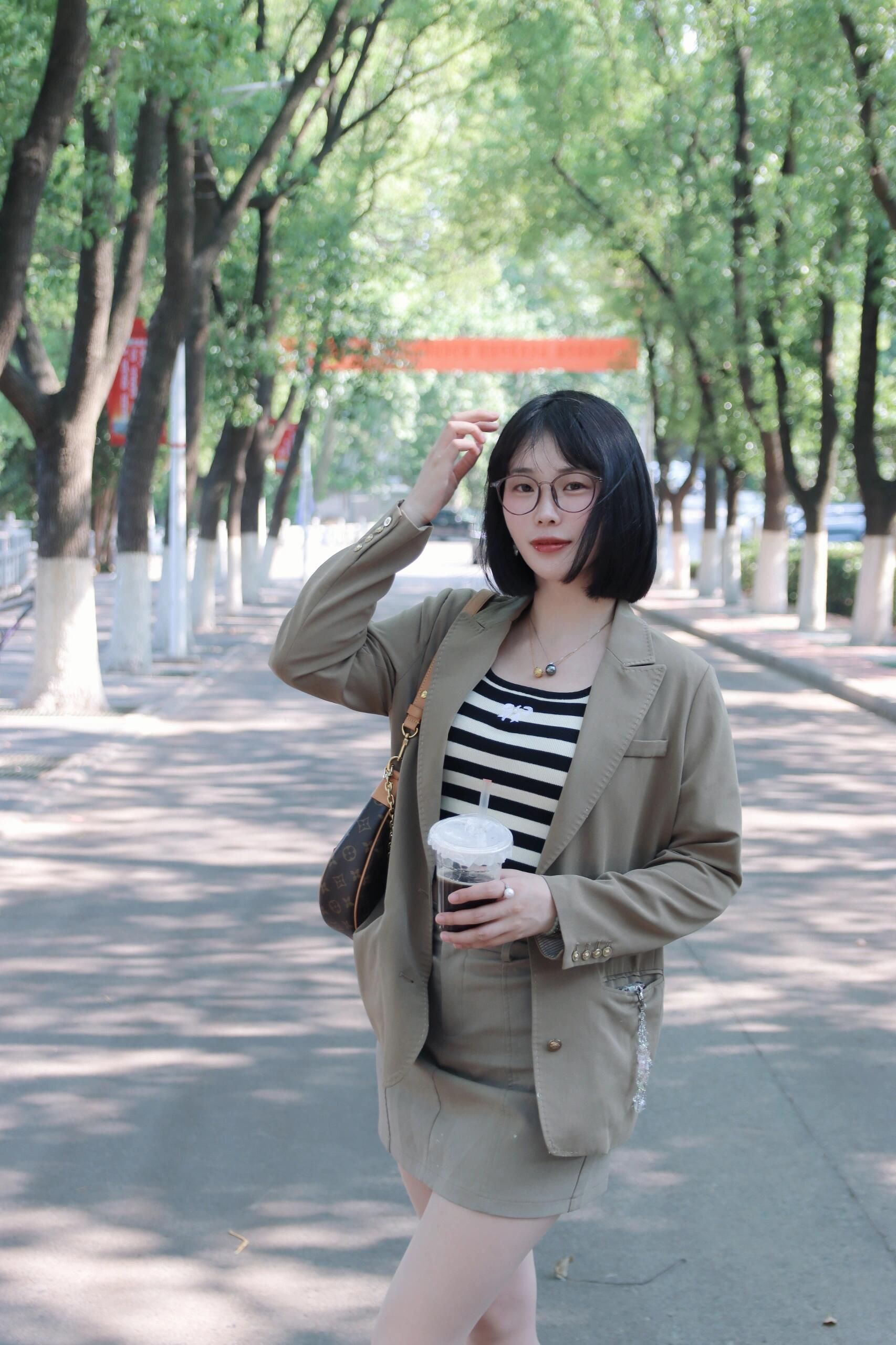 Stylish young woman in Nanjing park enjoying a sunny day with a beverage in hand. Summer fashion in China.
