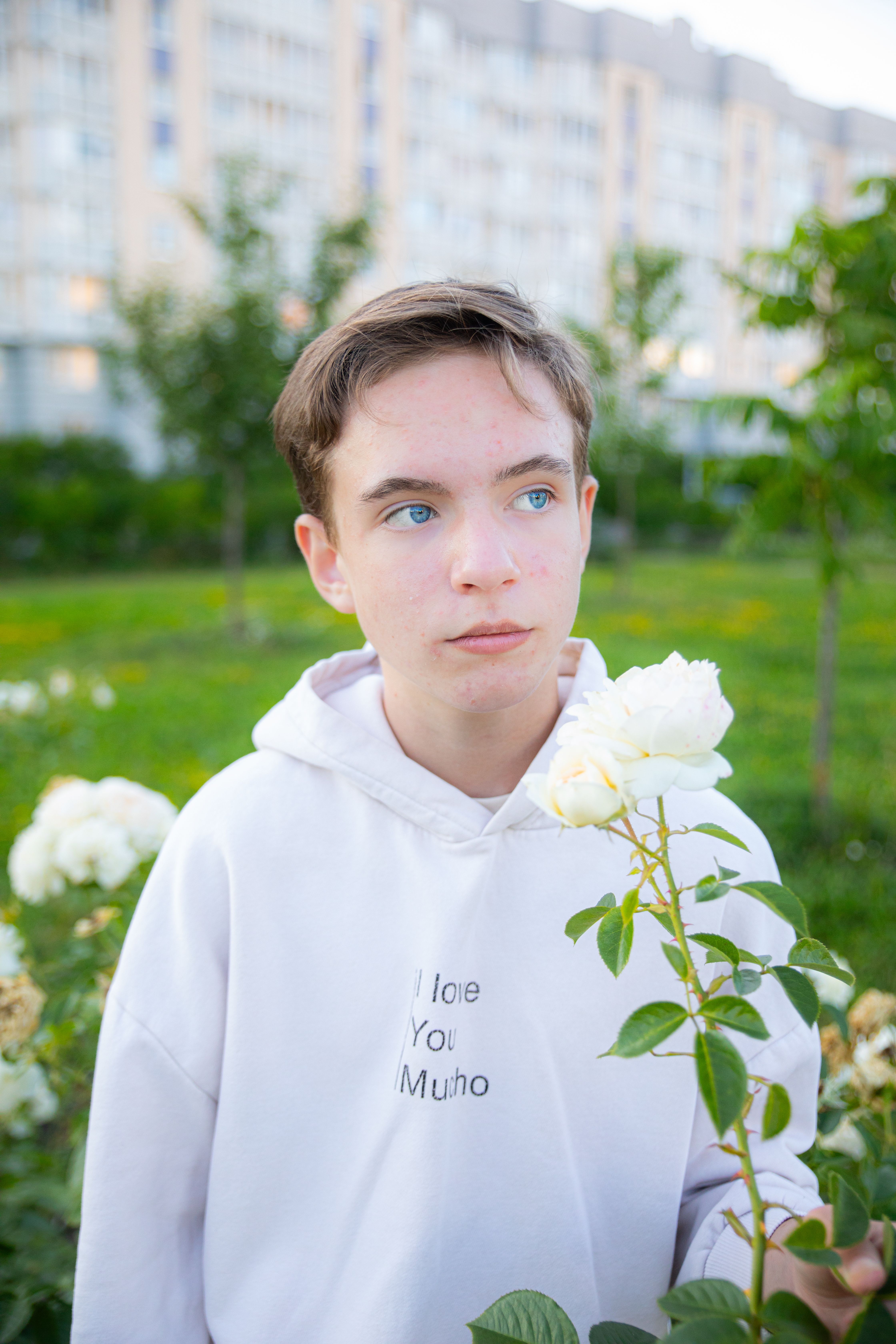 A young person in a hoodie near white roses in a city garden, showcasing urban nature.